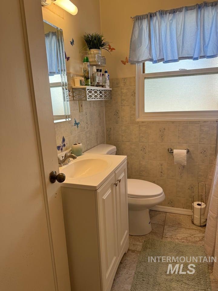 Bathroom featuring healthy amount of natural light, vanity, and tile walls