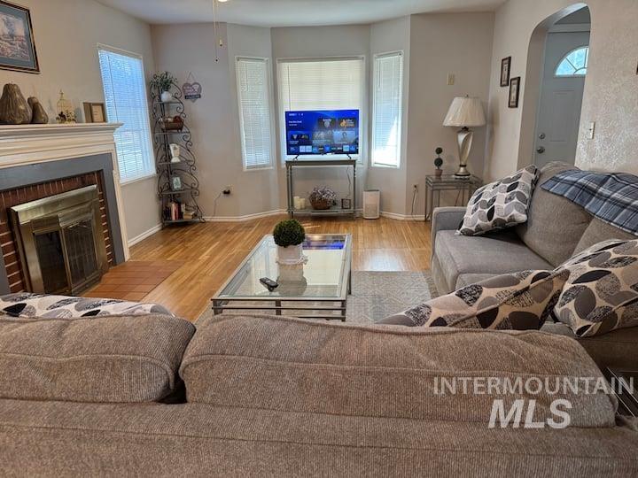 Living room with arched walkways, light wood-type flooring, and a brick fireplace