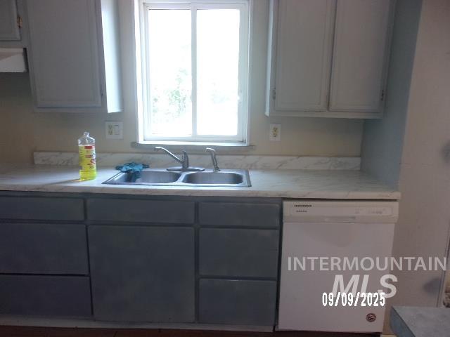 Kitchen with white dishwasher, light countertops, gray cabinetry, and extractor fan