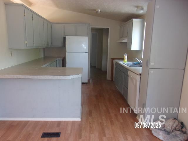 Kitchen with white appliances, lofted ceiling, light wood-type flooring, a textured ceiling, and light countertops