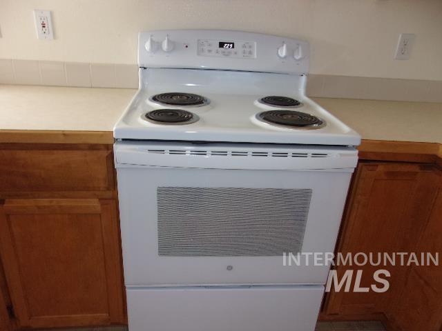 Kitchen view of white electric stove, brown cabinets, and light countertops