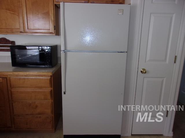 Kitchen featuring brown cabinetry, freestanding refrigerator, light countertops, and black microwave