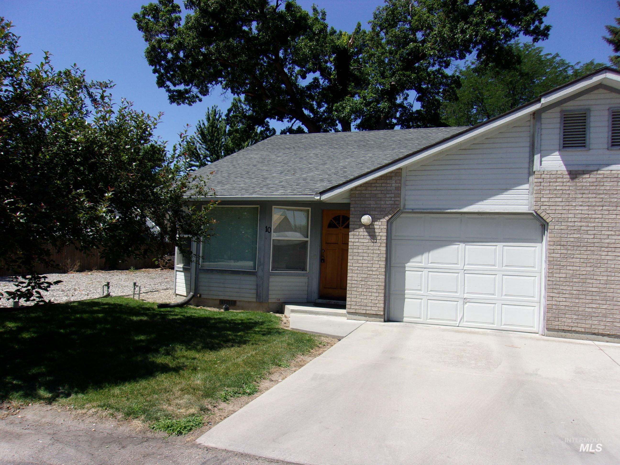 View of front facade featuring a front lawn, a garage, roof with shingles, driveway, and brick siding