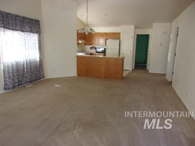 Kitchen with a peninsula, a chandelier, light carpet, freestanding refrigerator, and light countertops