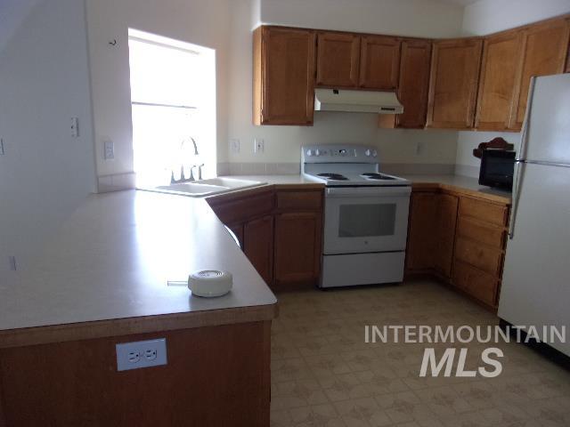 Kitchen featuring brown cabinetry, light countertops, white appliances, and light floors