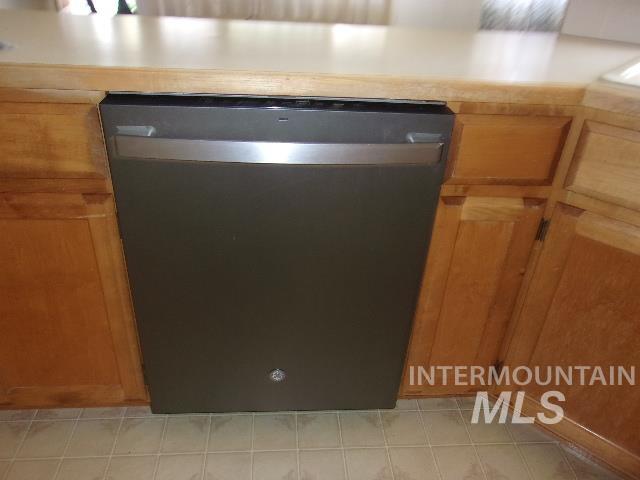 Kitchen view of stainless steel dishwasher, brown cabinets, and light countertops