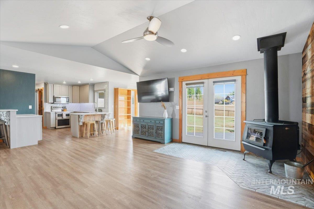 Living room with vaulted ceiling, a wood stove, french doors, light wood-style floors, and ceiling fan