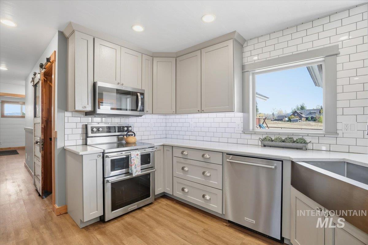 Kitchen with stainless steel appliances, light stone counters, light wood-type flooring, gray cabinets, and decorative backsplash
