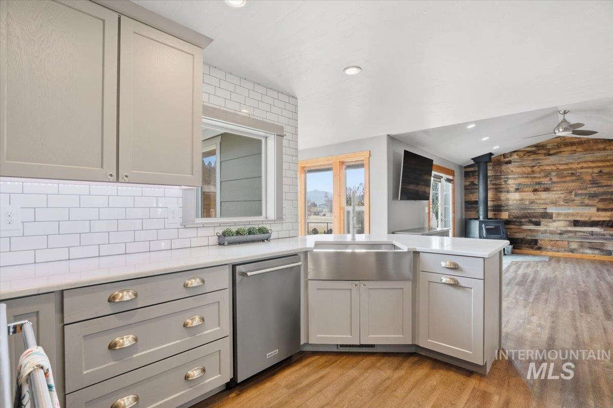 Kitchen with wood walls, a wood stove, gray cabinetry, stainless steel dishwasher, and lofted ceiling