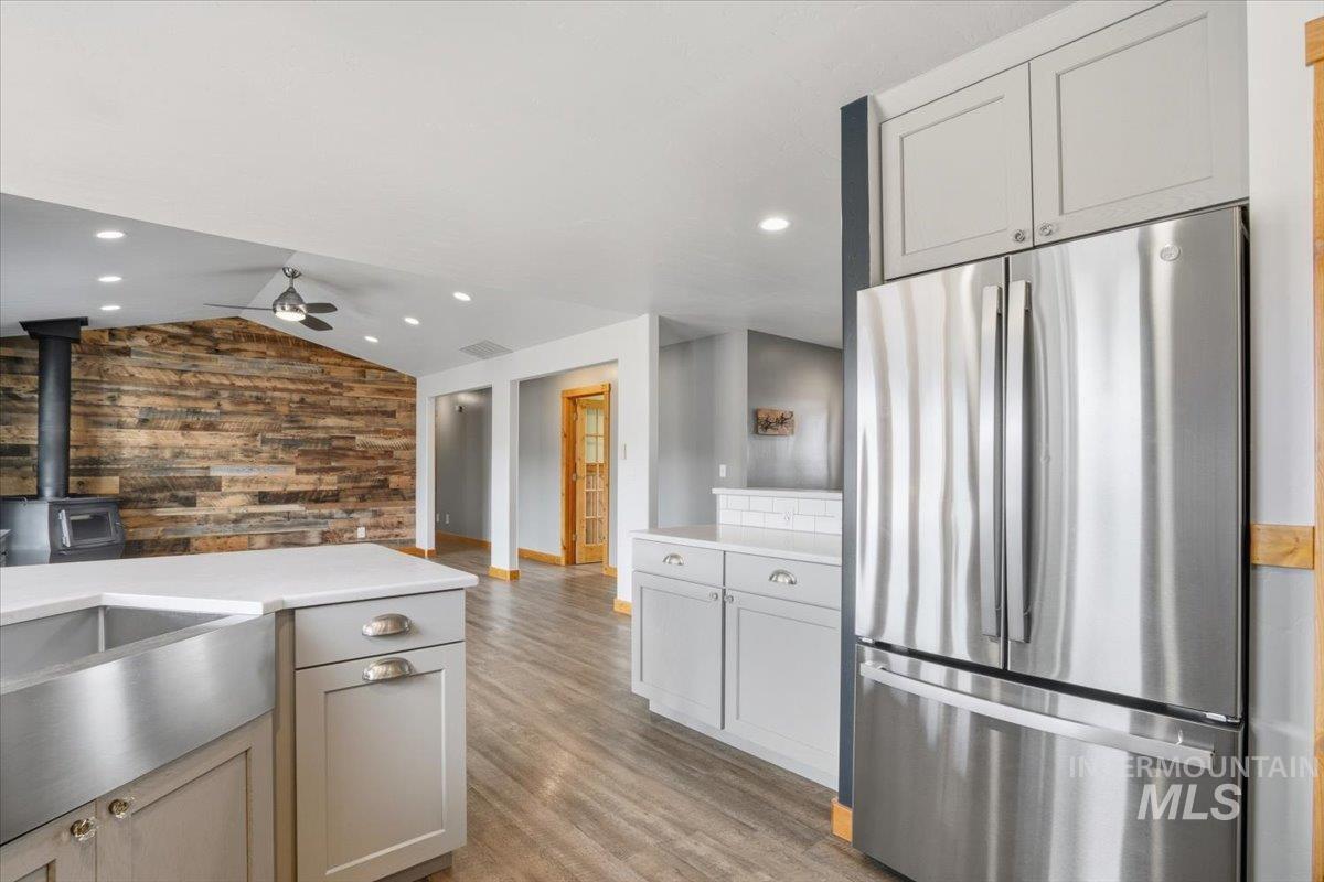 Kitchen with freestanding refrigerator, a wood stove, light wood finished floors, vaulted ceiling, and wooden walls