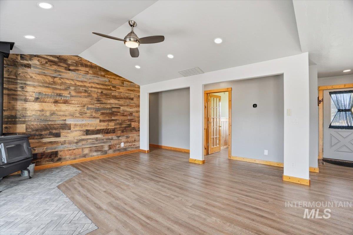 Unfurnished living room featuring wood walls, a wood stove, lofted ceiling, light wood-type flooring, and recessed lighting