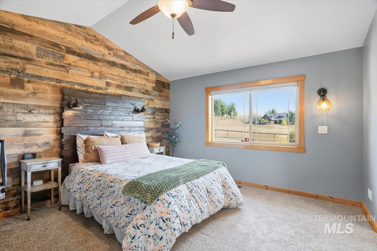 Bedroom with wood walls, lofted ceiling, carpet flooring, and a ceiling fan