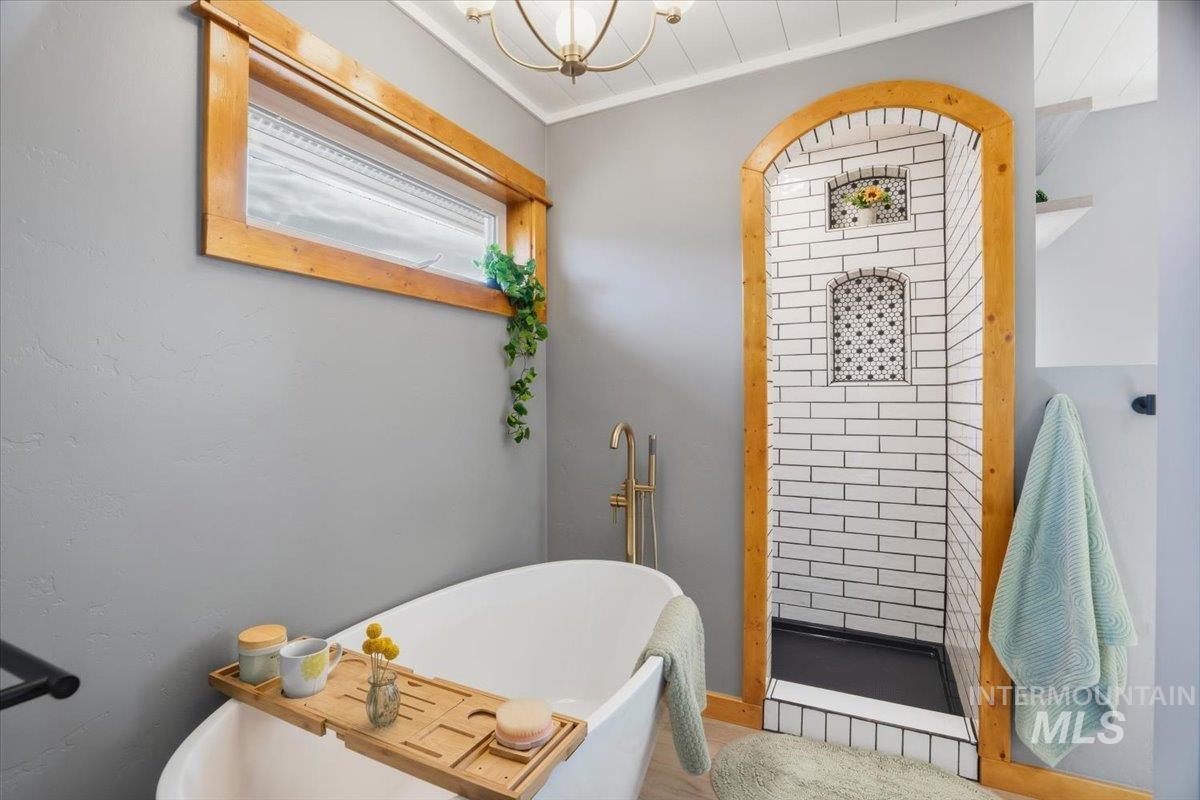Bathroom with a freestanding tub, a stall shower, crown molding, and a chandelier