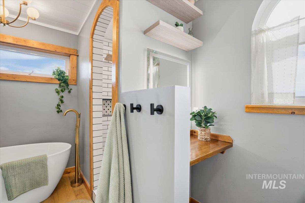 Bathroom featuring a freestanding bath, wood finished floors, a chandelier, a walk in shower, and crown molding