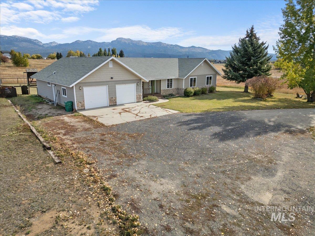 Single story home with a mountain view, driveway, stone siding, a garage, and a front lawn