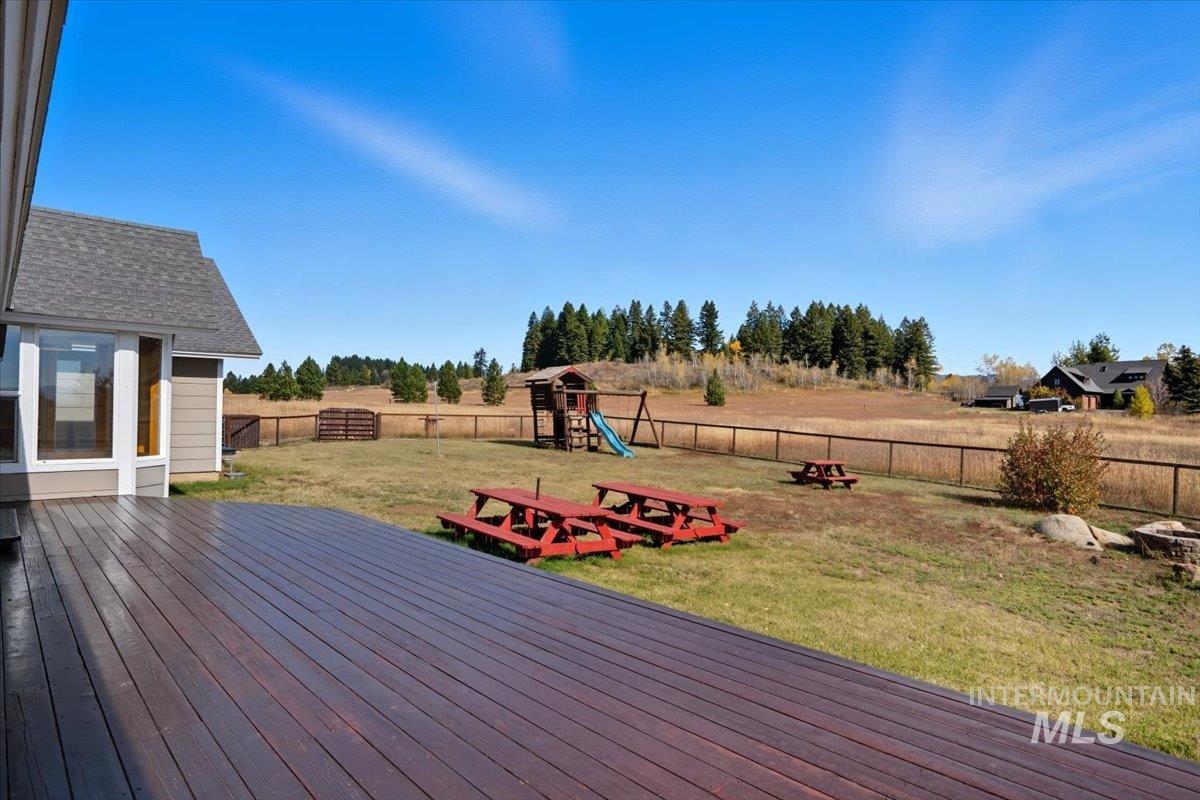 Deck featuring a fenced backyard, a playground, a view of countryside, and view of scattered trees