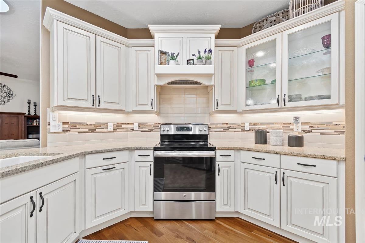 Kitchen with electric range, backsplash, white cabinets, light stone counters, and light wood-style floors