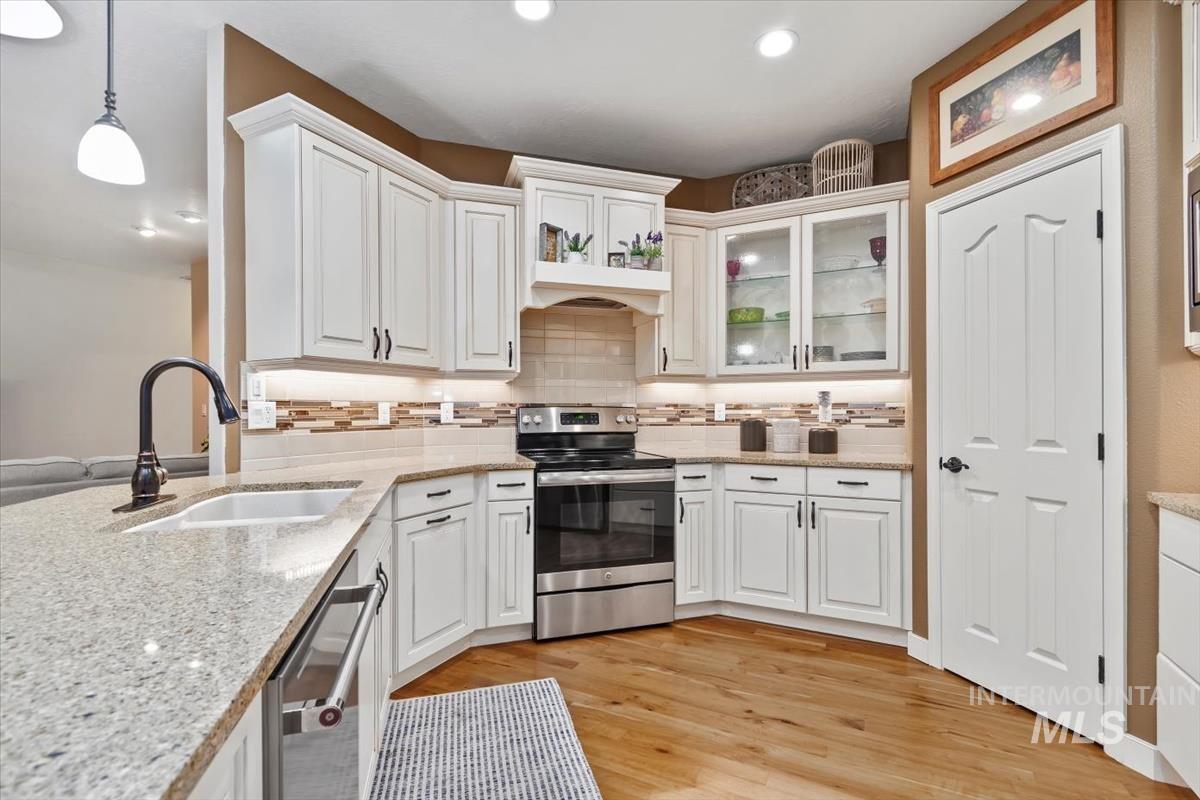 Kitchen featuring tasteful backsplash, stainless steel appliances, light wood finished floors, light stone counters, and hanging light fixtures