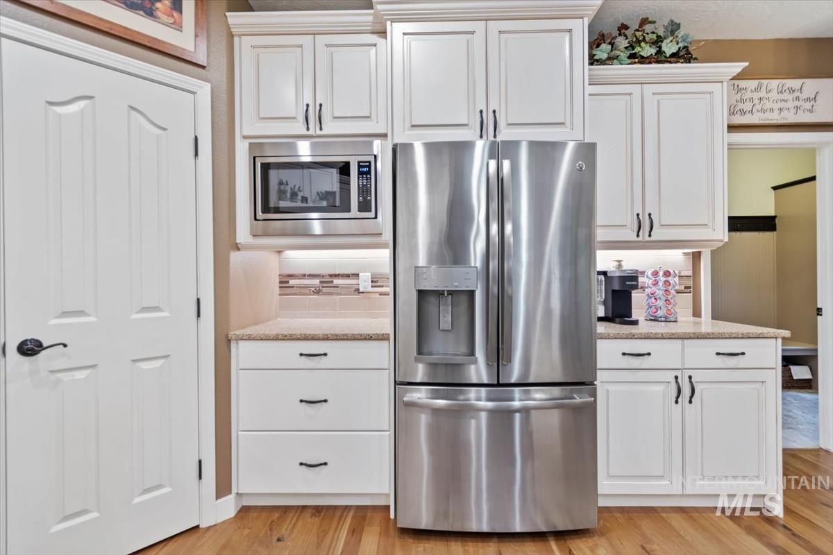 Kitchen with stainless steel appliances, white cabinets, tasteful backsplash, light stone countertops, and light wood-type flooring