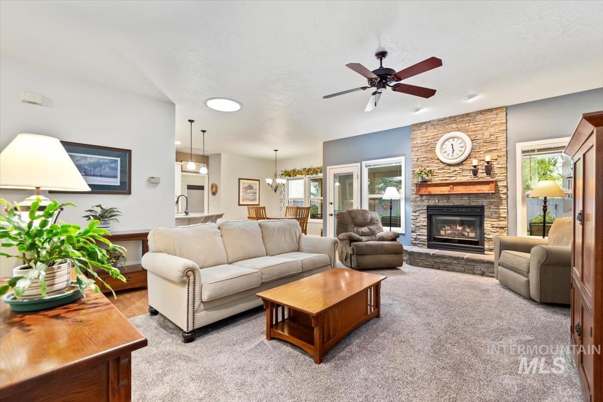 Living room featuring a stone fireplace, a chandelier, plenty of natural light, and a ceiling fan