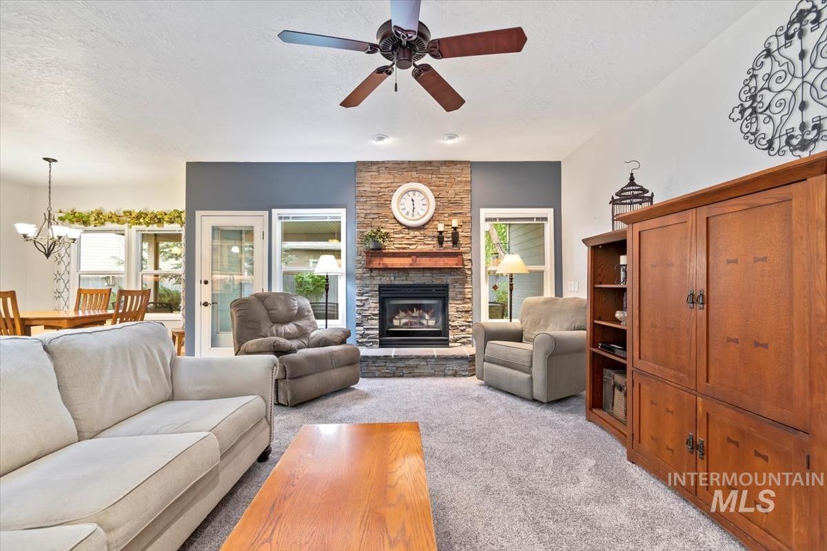 Carpeted living room featuring a fireplace, a textured ceiling, a ceiling fan, and a chandelier