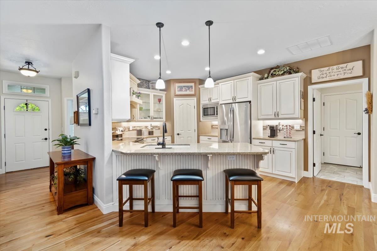 Kitchen with glass insert cabinets, a kitchen breakfast bar, a peninsula, light wood-style floors, and stainless steel appliances