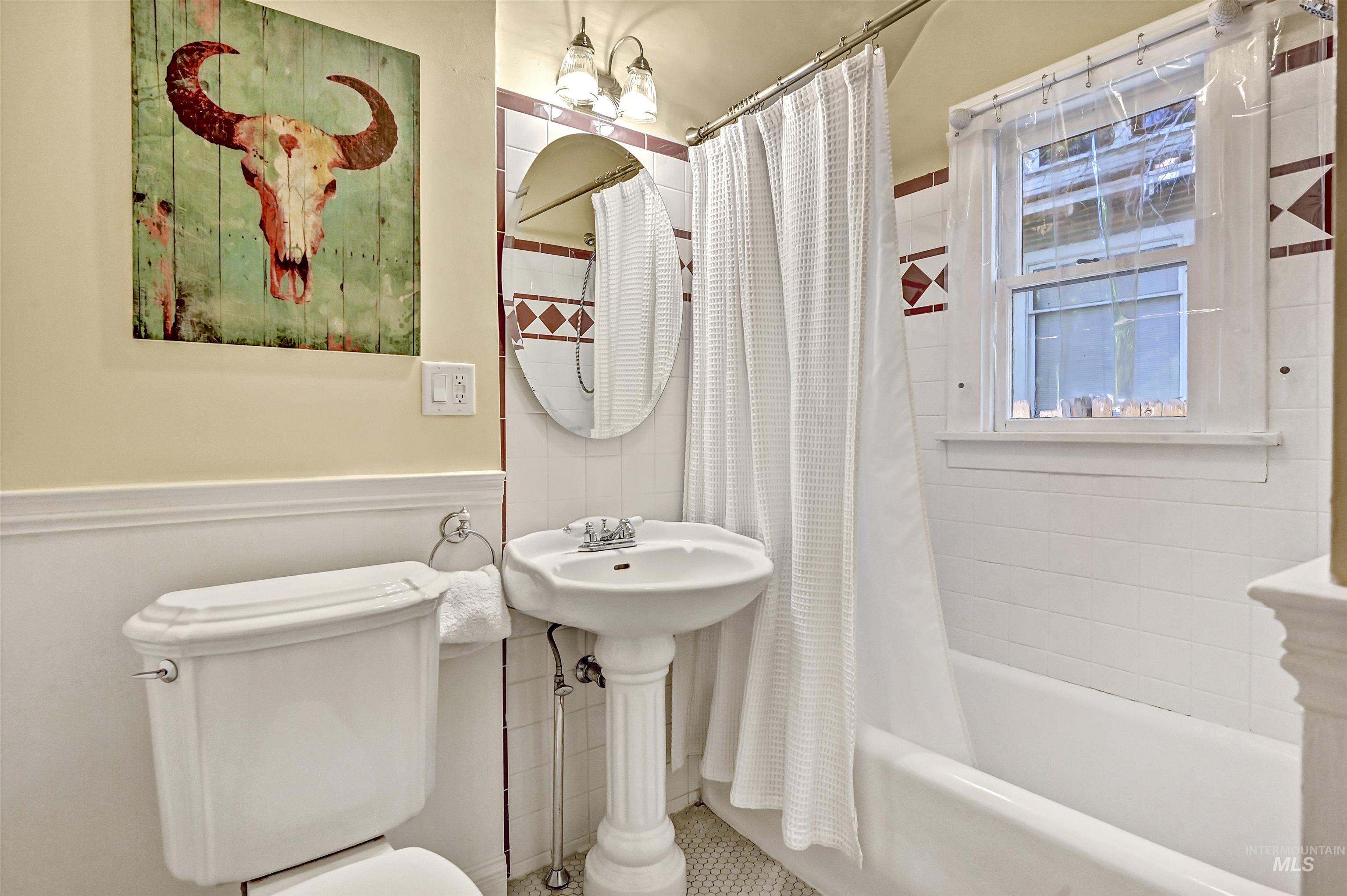 Charming bathroom with classic tile, pedestal sink & a window that brings in natural light.