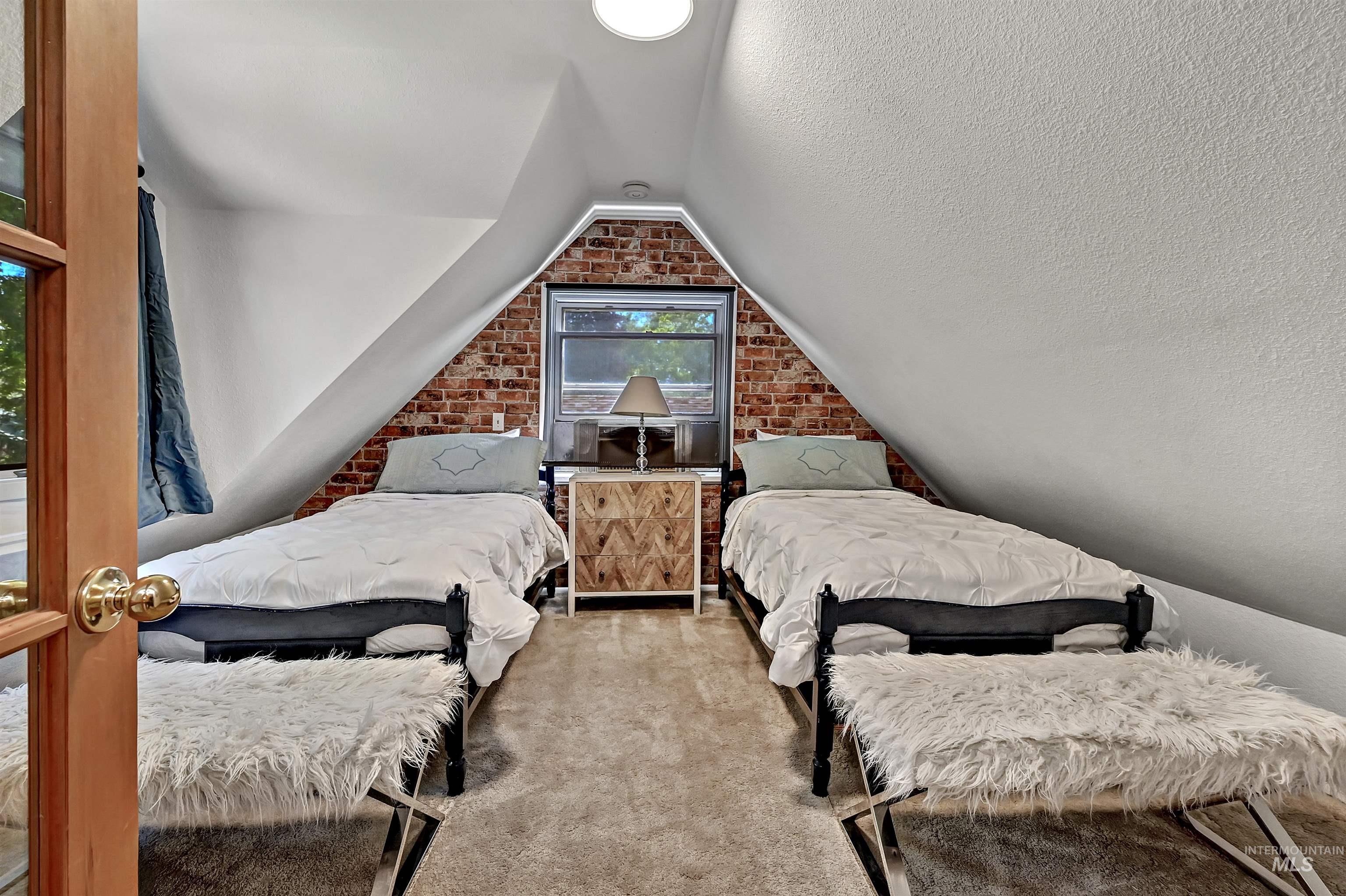 Inviting attic bedroom with vaulted ceiling, dormer window & a faux-brick accent wall that adds warmth & character.