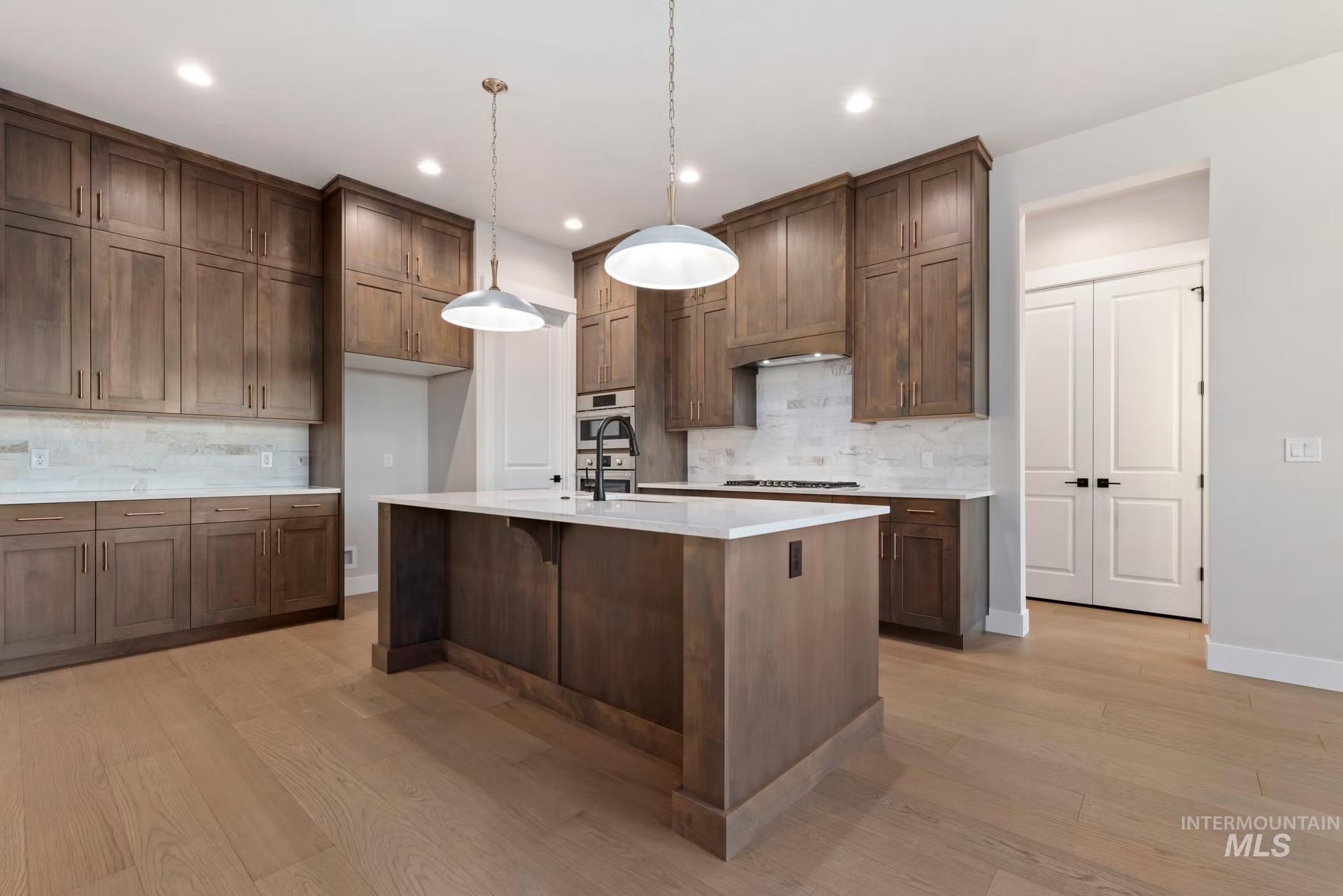 Kitchen featuring decorative light fixtures, backsplash, a breakfast bar area, light stone counters, and light wood-type flooring