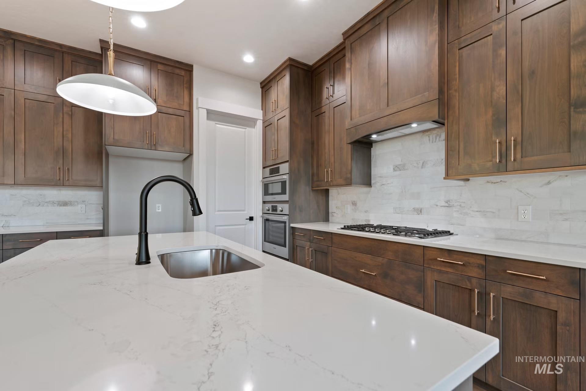 Kitchen featuring decorative light fixtures, tasteful backsplash, light stone counters, recessed lighting, and stainless steel appliances
