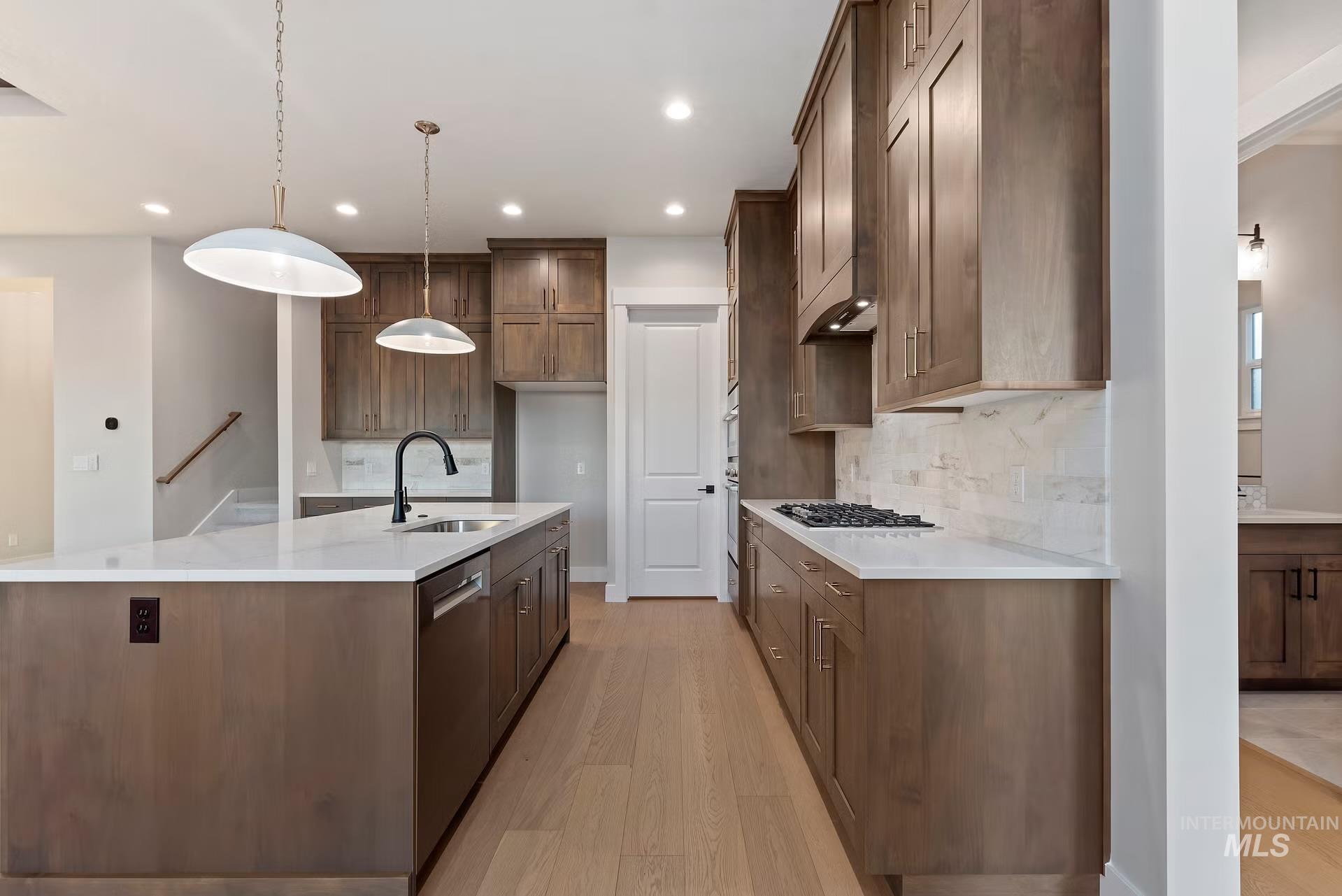 Kitchen featuring light wood-style flooring, decorative light fixtures, a large island with sink, light stone countertops, and recessed lighting