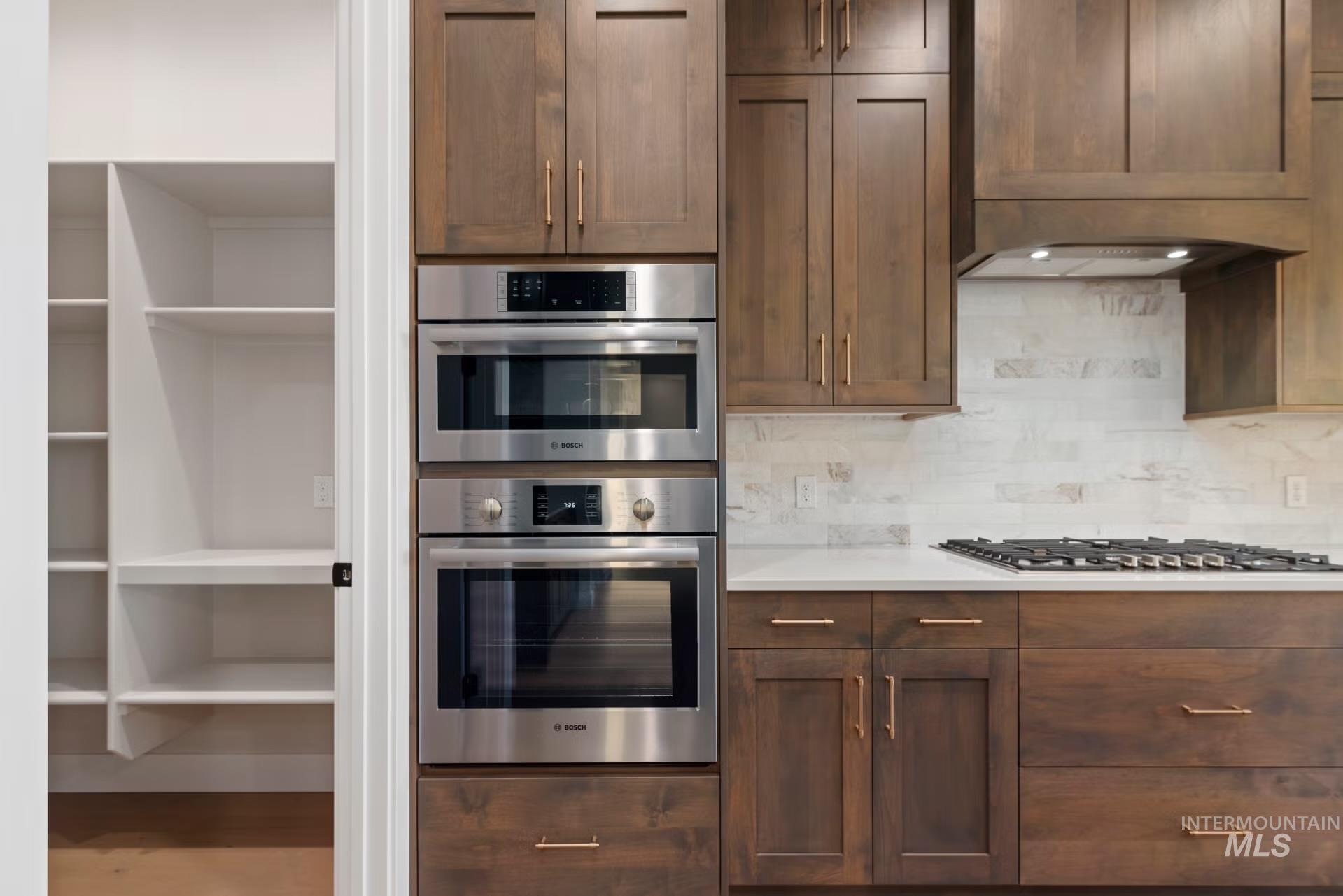 Kitchen featuring appliances with stainless steel finishes, tasteful backsplash, dark brown cabinetry, and light stone counters