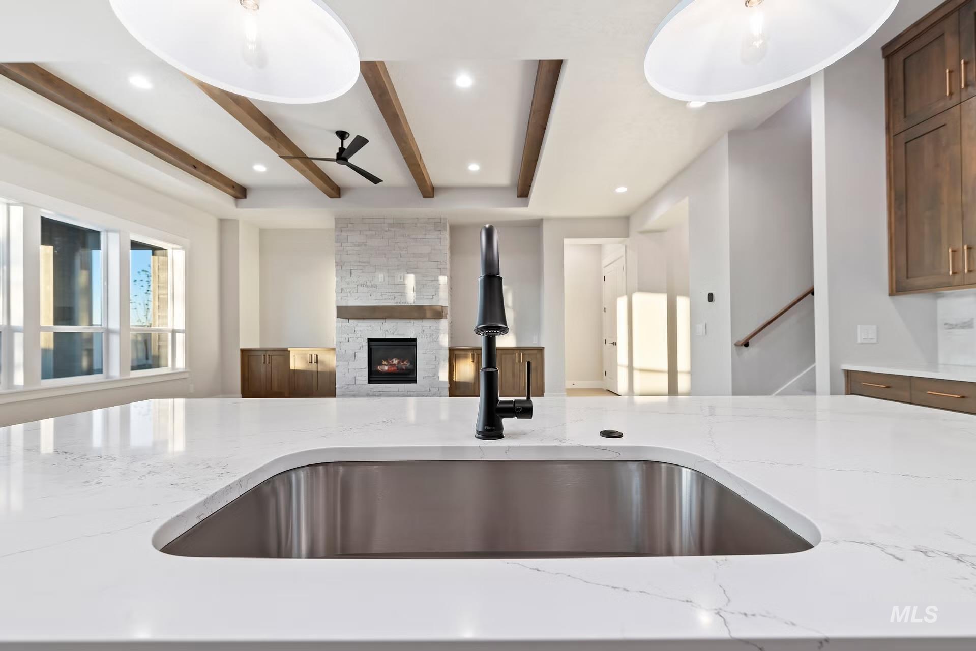 Kitchen featuring light stone counters, open floor plan, beam ceiling, a ceiling fan, and a fireplace