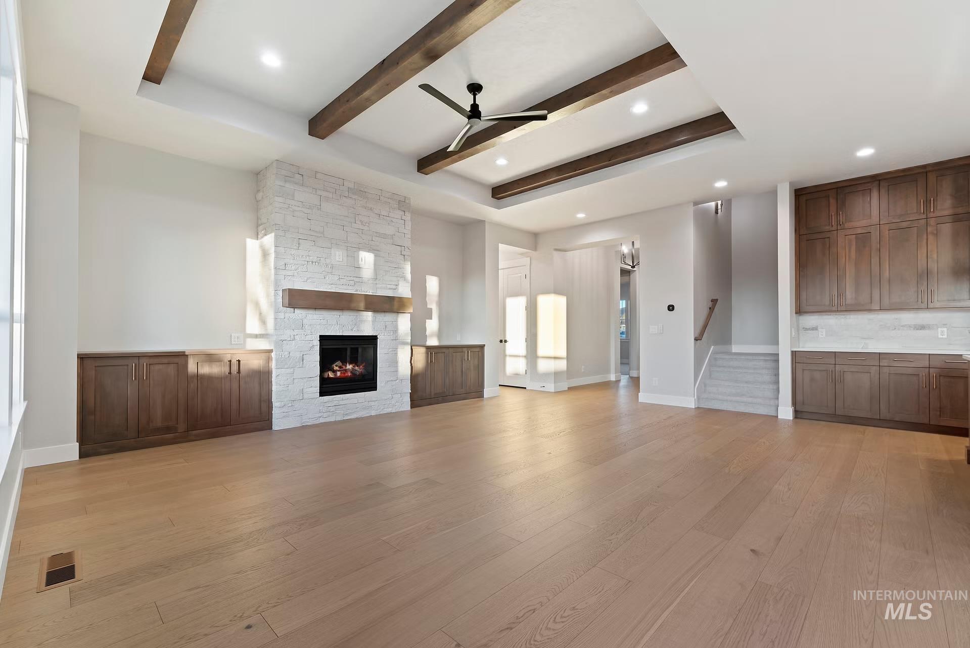 Unfurnished living room with light wood-style flooring, a ceiling fan, a fireplace, stairway, and beam ceiling