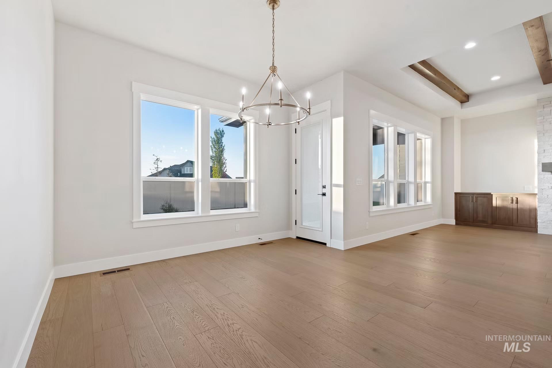 Unfurnished dining area featuring a chandelier, light wood finished floors, a raised ceiling, and recessed lighting