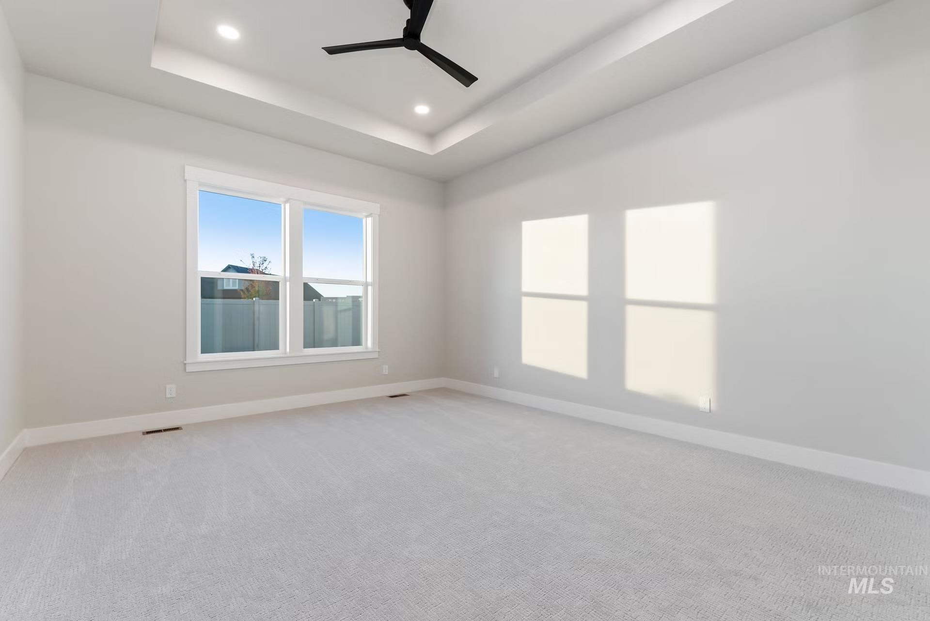 Unfurnished room featuring a raised ceiling, light colored carpet, recessed lighting, and a ceiling fan