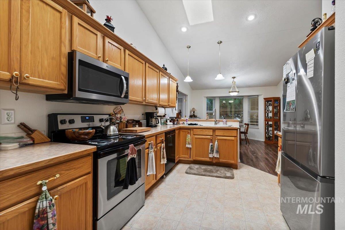 Kitchen featuring appliances with stainless steel finishes, cabinetry, light countertops and vaulted ceiling