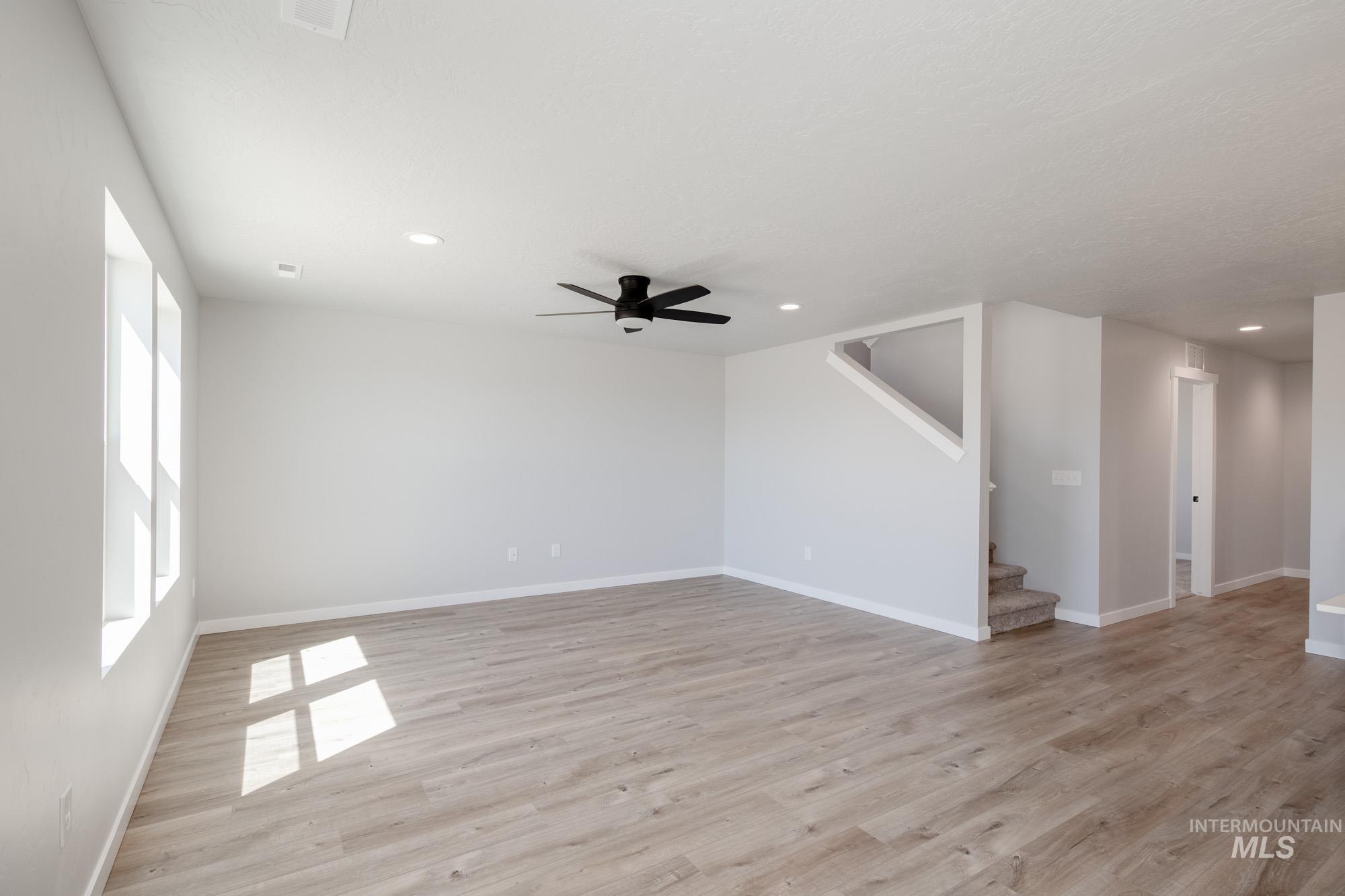 Unfurnished living room featuring light wood-style floors, a ceiling fan, recessed lighting, and stairs