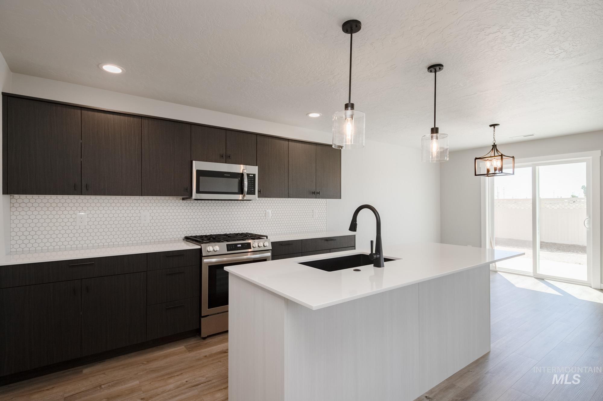 Kitchen featuring stainless steel appliances, modern cabinets, backsplash, light wood-type flooring, and hanging light fixtures