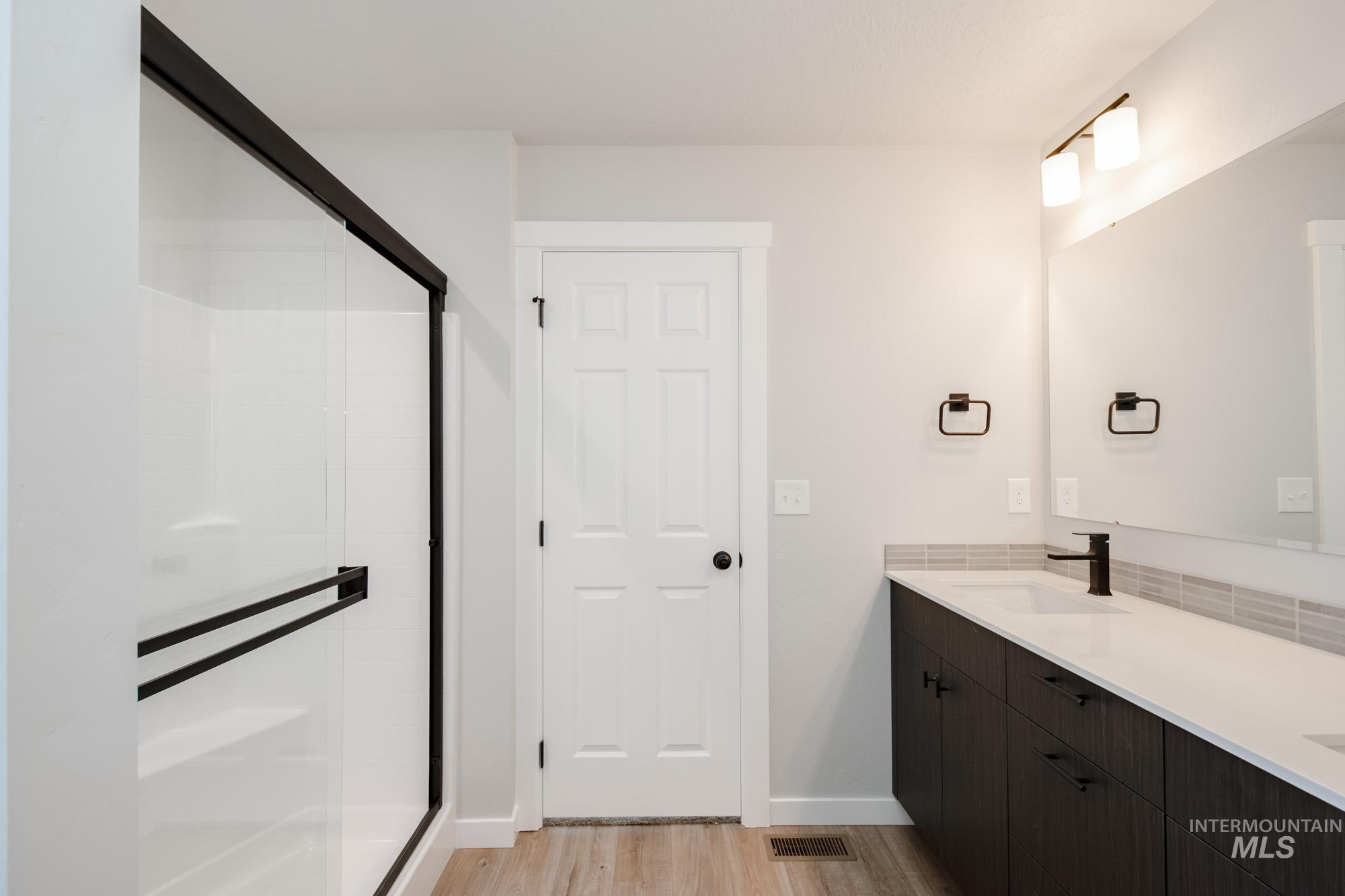 Bathroom with a stall shower, light wood-style flooring, and double vanity