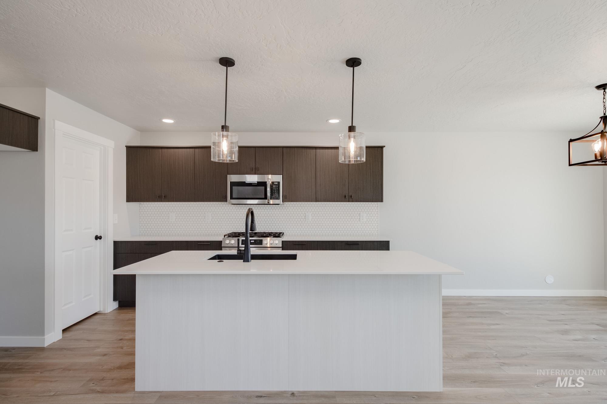 Kitchen featuring decorative light fixtures, tasteful backsplash, dark brown cabinets, a textured ceiling, and recessed lighting