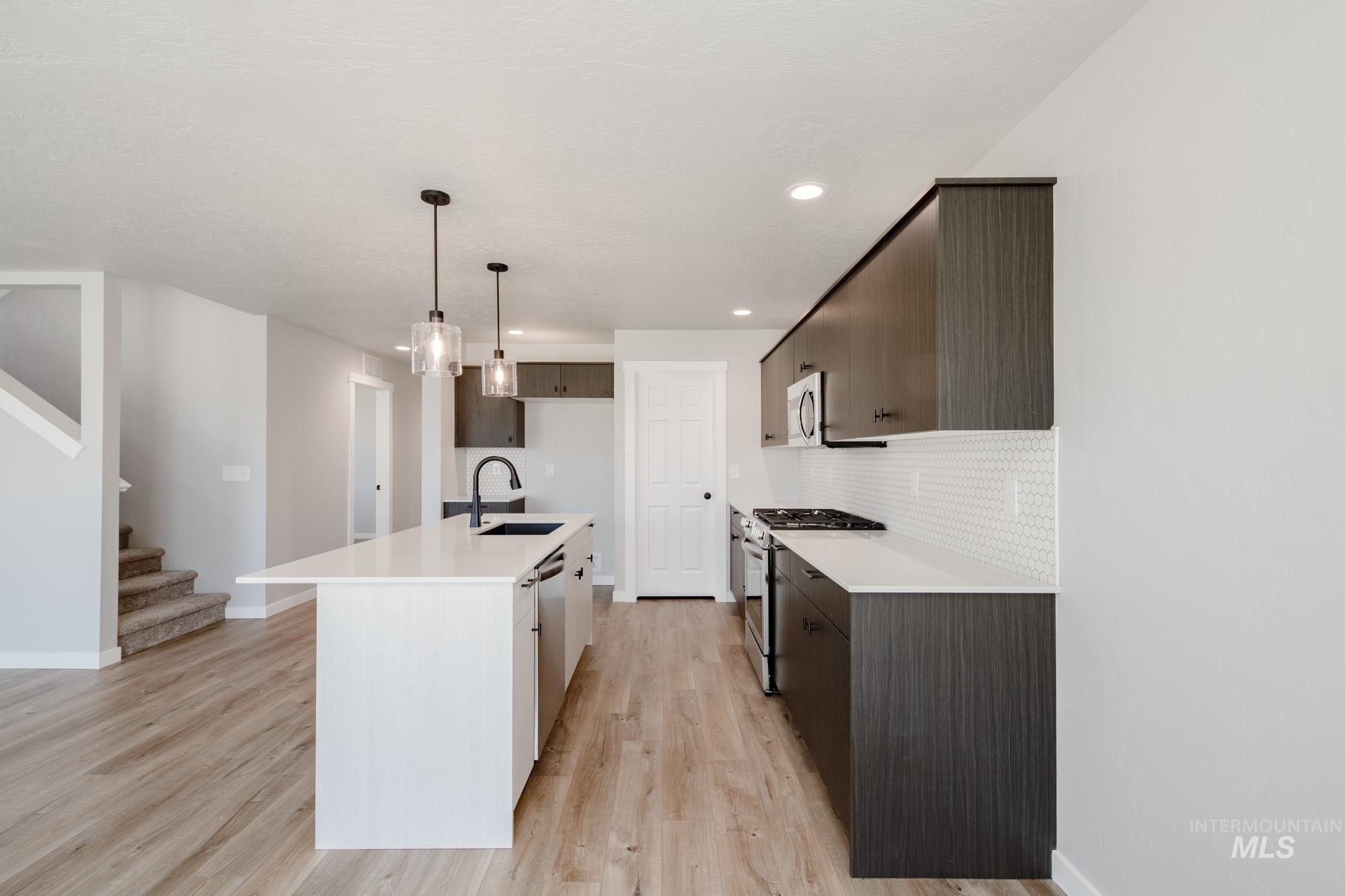 Kitchen with dark brown cabinetry, a center island with sink, appliances with stainless steel finishes, light wood-type flooring, and recessed lighting