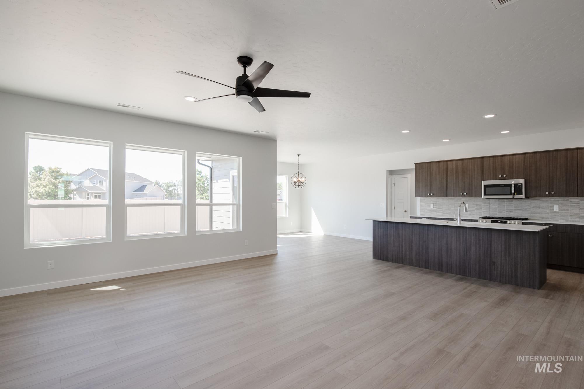 Kitchen with open floor plan, a center island with sink, tasteful backsplash, dark brown cabinetry, and a ceiling fan