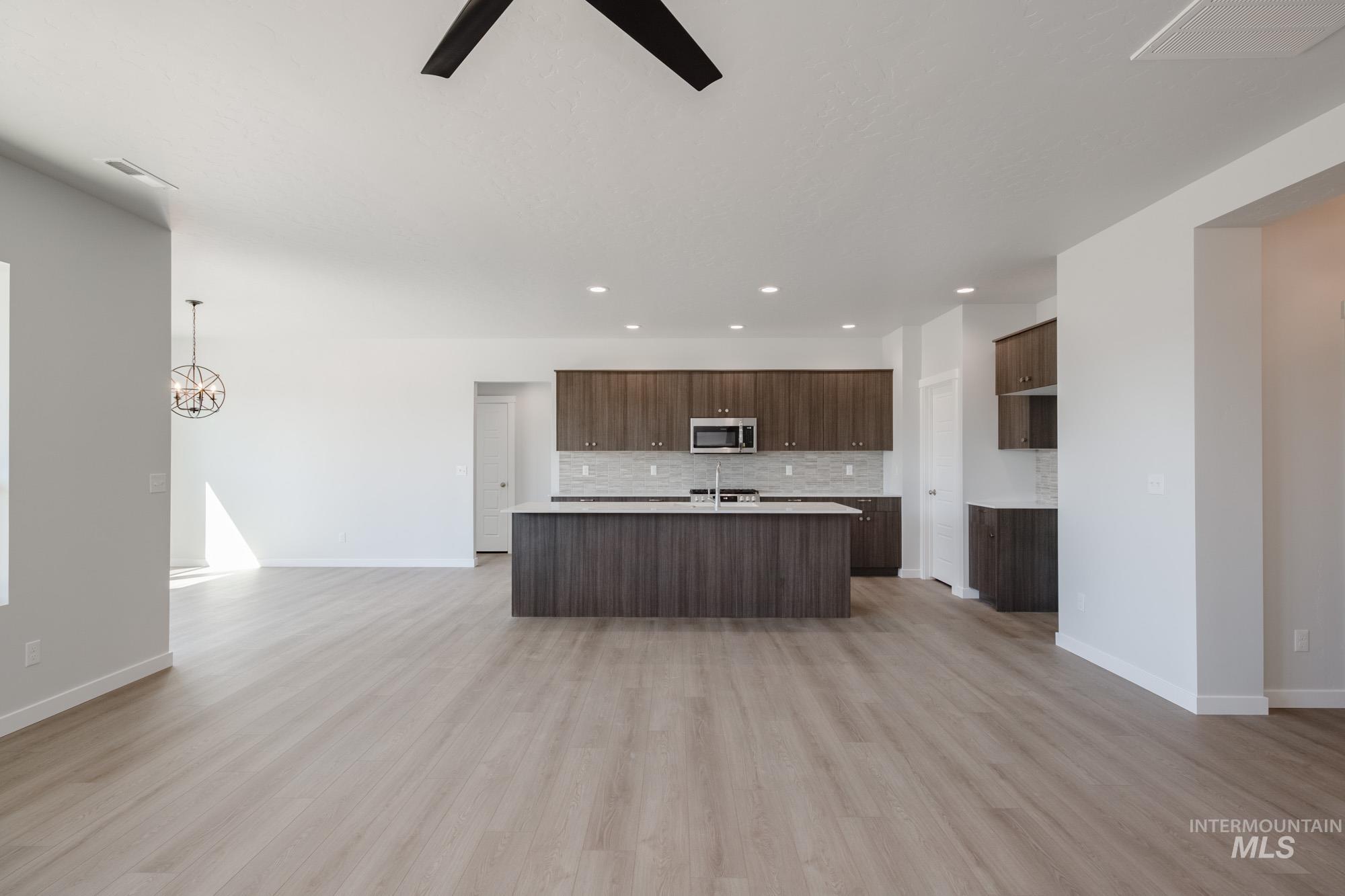 Kitchen featuring open floor plan, backsplash, light wood-style flooring, dark brown cabinets, and a center island with sink