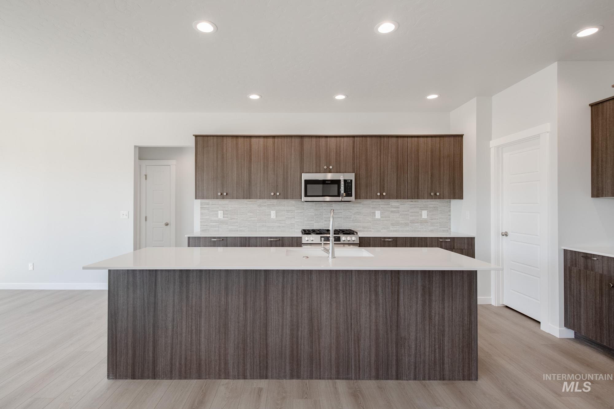 Kitchen with decorative backsplash, an island with sink, recessed lighting, modern cabinets, and appliances with stainless steel finishes