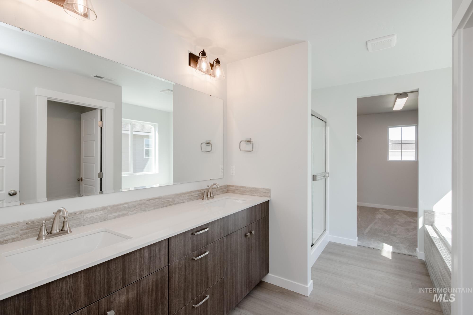 Full bath with double vanity, light wood-style flooring, a stall shower, and a garden tub