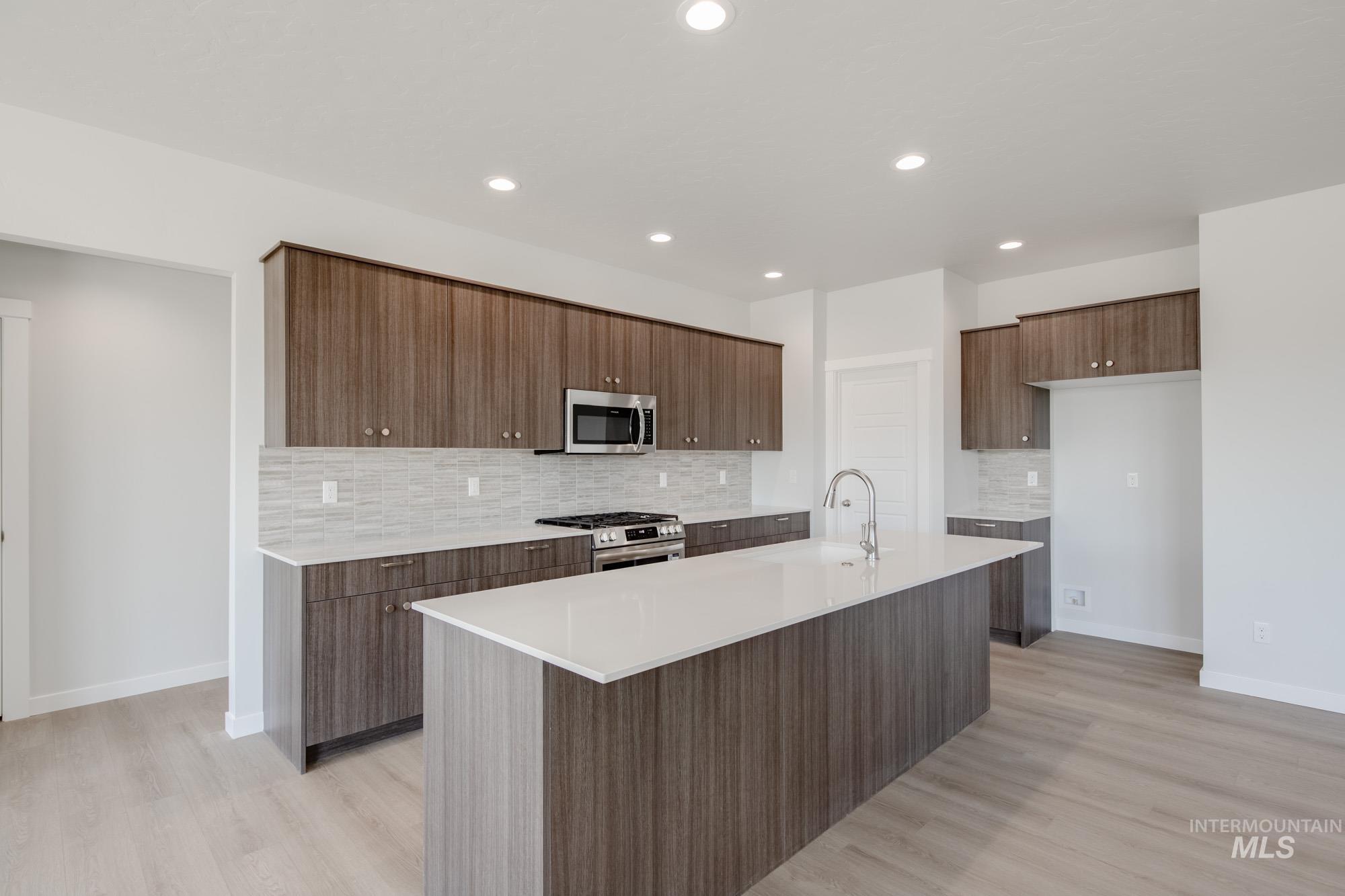 Kitchen with backsplash, appliances with stainless steel finishes, modern cabinets, light wood-style floors, and recessed lighting