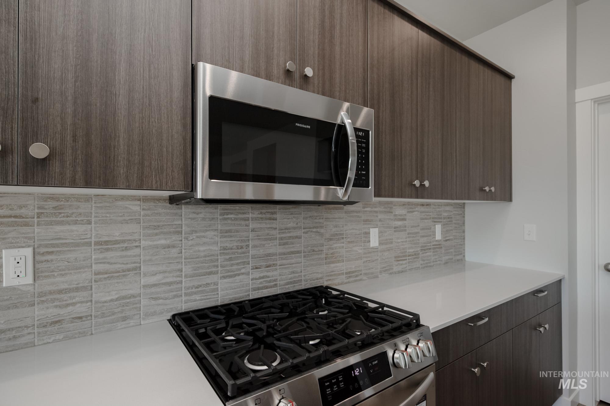 Kitchen with stainless steel appliances, modern cabinets, dark brown cabinets, backsplash, and light stone countertops