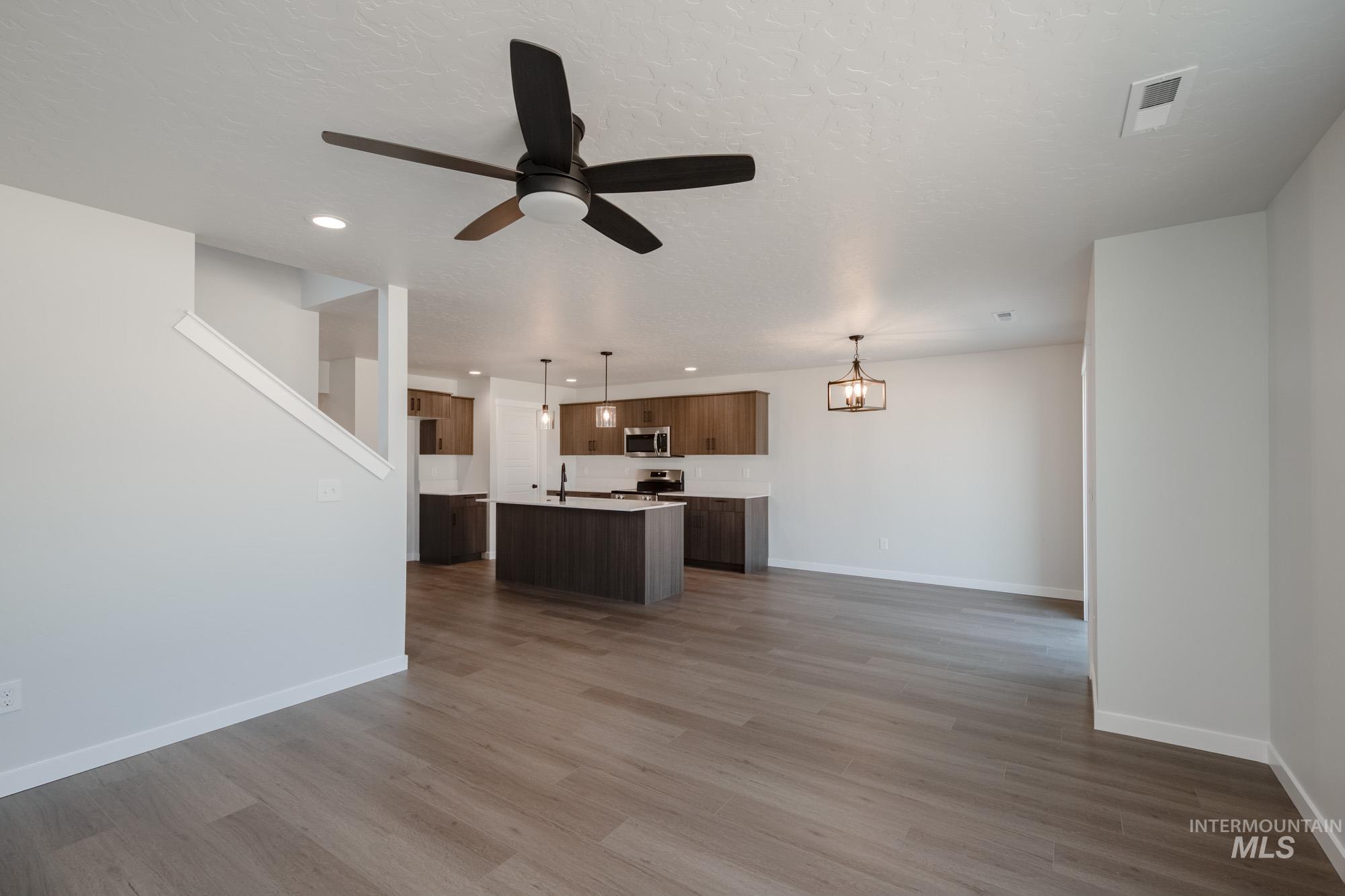Unfurnished living room with light wood-type flooring, a ceiling fan, recessed lighting, a textured ceiling, and a chandelier