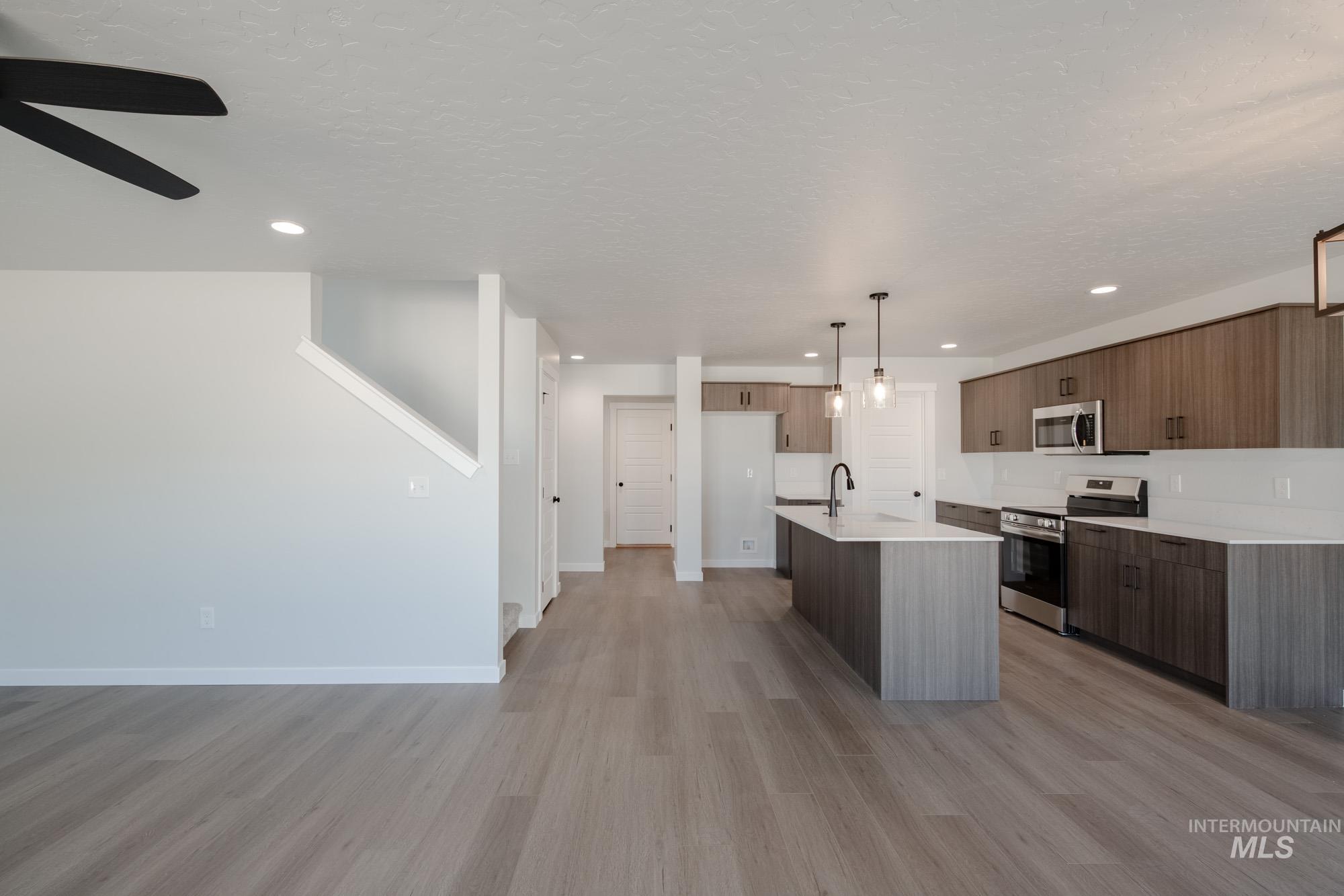 Kitchen featuring stainless steel appliances, light wood-style flooring, decorative light fixtures, recessed lighting, and a center island with sink